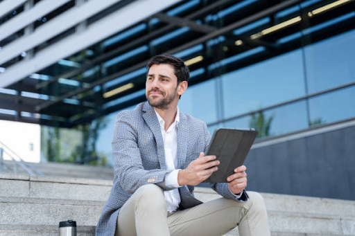 A businessman sits on outdoor steps, holding a tablet, representing analysis of RAK Free Zone license costs.